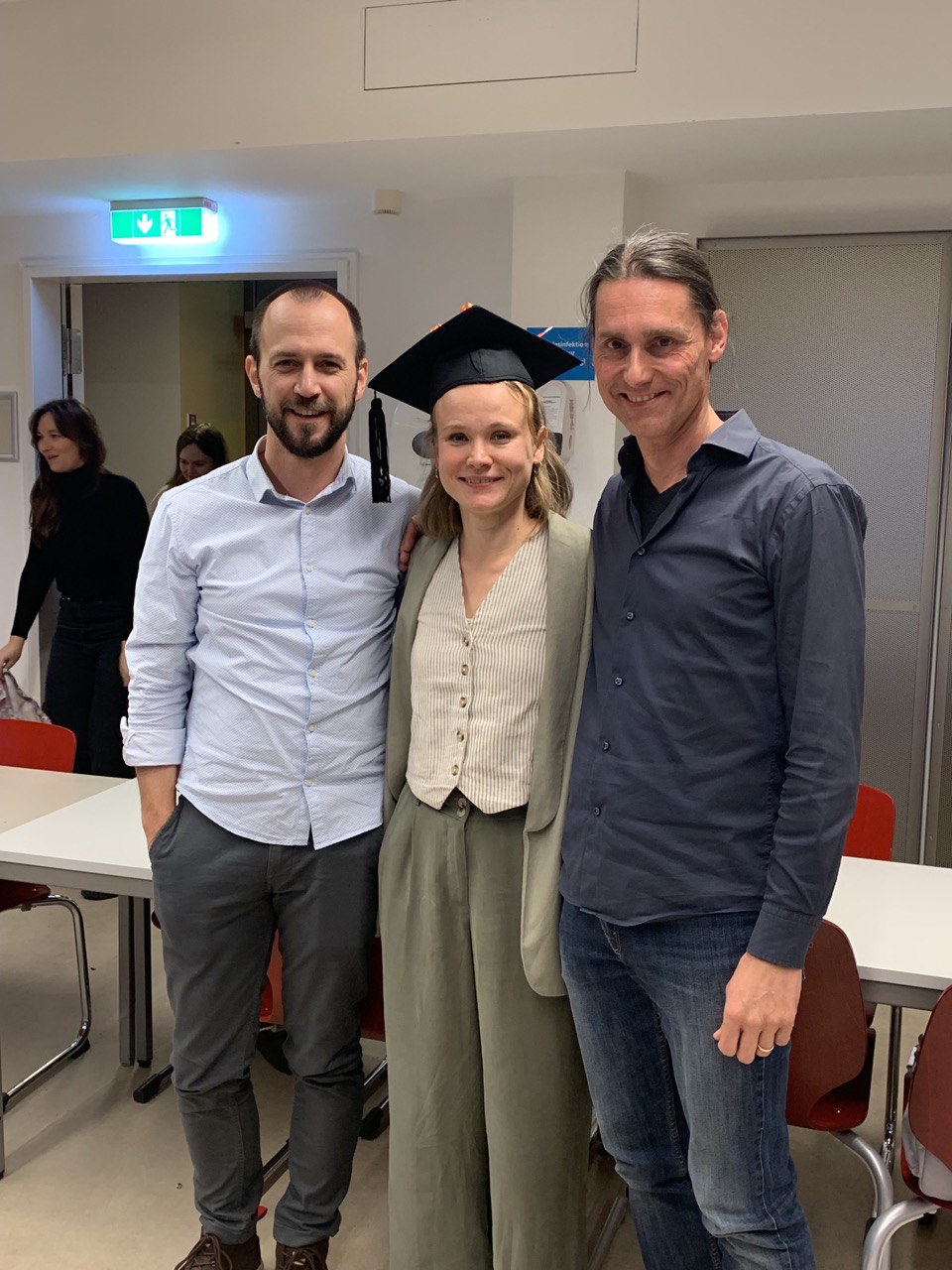 Three people are standing next to each other. In the middle: Karoline Thorbecke wearing a decorated mortar board. On her left, David Gerlach. On her right: Andreas Bonnet. All three are smiling.